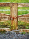 Old rusty padlock on a metal chain on a wooden gate. Green field in the background. Concept security of farmland and private Royalty Free Stock Photo