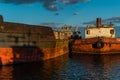 Old rusty red brown barges at sea, reflected in blue water in sunset light. Beautiful seascape with abandoned boats Royalty Free Stock Photo