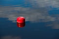 An old and rusty red buoy, stained with bird droppings. Red buoy in the water with cloudy sky reflected in it Royalty Free Stock Photo