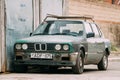 Old rusty sedan car BMW 3 Series (E30) parking on street. The BMW E30 is an entry-level luxury car which was produced by