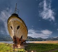 Old rusty ship on a slipway on the shore of a lake against a blue sky with high clouds