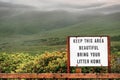 Old rusty sign with message keep this area beautiful, bring your litter home. Green mountains in the background covered with low