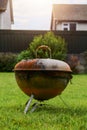 Old rusty small barbeque cooker in a garden. Cheap metal cooking device. Worn out budget way to cook food