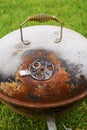 Old rusty small barbeque cooker in a garden. Cheap metal cooking device. Worn out budget way to cook food Royalty Free Stock Photo