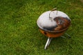 Old rusty small barbeque cooker in a garden. Cheap metal cooking device. Worn out budget way to cook food