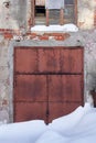 old rusty snow-covered gate in the wall of an abandoned industrial building. The entrance is closed and blocked