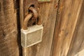 Old rusty squre padlock hanging on brown wooden door Royalty Free Stock Photo