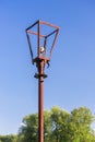 Old rusty street lamp with broken bulb and torn electrical wires against bright, summer blue sky and green trees. Devastation and Royalty Free Stock Photo