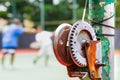 Old and rustic tennis net reel post with blurred persons taking tennis lesson on the background Royalty Free Stock Photo