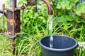 old rusty water column in the village fills the bucket with water on the background of dense grass and trees