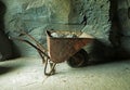 Old rusty wheelbarrow with ore at the mine at stone wall Royalty Free Stock Photo