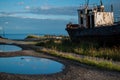 old rusty white ship, boat on grassy shore in light of sun, near round puddles on coast of lake Baikal,