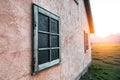 Old rusty wooden frame on stone painted pink wall on mountain house at sunset time.