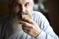 Old sad man with a long gray beard sitting by the table and eating bread Royalty Free Stock Photo