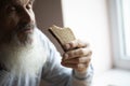 Old sad man with a long gray beard sitting by the table and eating bread Royalty Free Stock Photo