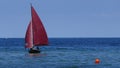 Small sailboat, an old sailing dinghy with dark red sails floats in the blue sea Royalty Free Stock Photo