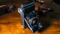 Old scratched and dusty antique photo camera, with foldable original Carl Zeiss Lens, on a rustic wooden table.