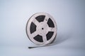 Old scratched metal reel with audio or video tape on a gray studio background. Bobbin, retro magnetic spool. Round reel