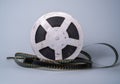 Old scratched metal reel with audio or video tape on a gray studio background. Bobbin, retro magnetic spool. Round reel