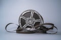 Old scratched metal reel with audio or video tape on a gray studio background. Bobbin, retro magnetic spool. Round reel