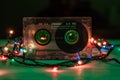 An old, scratched RAKS audiotape stands on a green background, festooned with multicolored lights