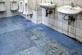 Old scruffy toilet where the floor is wet and filled with dirty footprints of student,filthy of urinals,washbasin,tiled wall,