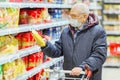 Old senior european man wearing protective facial mask looking at groceries in the supermarket. Shopping during COVID-19 concept