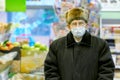 Old senior european man wearing protective facial mask in warm jacket and cap in the supermarket. Shopping during COVID-19 concept