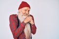 Old senior man with grey hair and long beard wearing hipster look with wool cap laughing nervous and excited with hands on chin Royalty Free Stock Photo