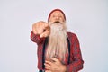 Old senior man with grey hair and long beard wearing hipster look with wool cap laughing at you, pointing finger to the camera Royalty Free Stock Photo