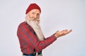 Old senior man with grey hair and long beard wearing hipster look with wool cap pointing aside with hands open palms showing copy Royalty Free Stock Photo