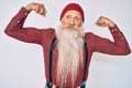 Old senior man with grey hair and long beard wearing hipster look with wool cap showing arms muscles smiling proud
