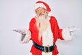 Old senior man with grey hair and long beard wearing santa claus costume clueless and confused expression with arms and hands Royalty Free Stock Photo