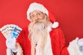 Old senior man with grey hair and long beard wearing santa claus costume holding canadian dollars celebrating achievement with
