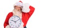 Old senior man with grey hair and long beard wearing santa claus costume holding clock stressed and frustrated with hand on head, Royalty Free Stock Photo