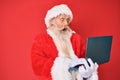 Old senior man with grey hair and long beard wearing santa claus costume using laptop celebrating crazy and amazed for success Royalty Free Stock Photo