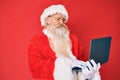 Old senior man with grey hair and long beard wearing santa claus costume using laptop depressed and worry for distress, crying Royalty Free Stock Photo