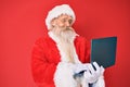 Old senior man with grey hair and long beard wearing santa claus costume using laptop smiling with a happy and cool smile on face Royalty Free Stock Photo