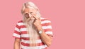 Old senior man with grey hair and long beard wearing striped tshirt pointing to the eye watching you gesture, suspicious Royalty Free Stock Photo