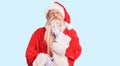 Old senior man with grey hair and long beard wearing traditional santa claus costume thinking concentrated about doubt with finger Royalty Free Stock Photo