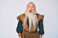 Old senior man with grey hair and long beard wearing viking traditional costume afraid and shocked with surprise and amazed