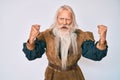 Old senior man with grey hair and long beard wearing viking traditional costume angry and mad raising fists frustrated and furious