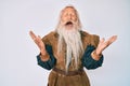 Old senior man with grey hair and long beard wearing viking traditional costume celebrating mad and crazy for success with arms