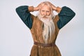 Old senior man with grey hair and long beard wearing viking traditional costume crazy and scared with hands on head, afraid and