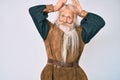Old senior man with grey hair and long beard wearing viking traditional costume doing bunny ears gesture with hands palms looking Royalty Free Stock Photo