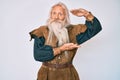 Old senior man with grey hair and long beard wearing viking traditional costume gesturing with hands showing big and large size