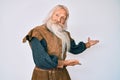 Old senior man with grey hair and long beard wearing viking traditional costume inviting to enter smiling natural with open hand