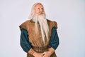 Old senior man with grey hair and long beard wearing viking traditional costume looking away to side with smile on face, natural Royalty Free Stock Photo