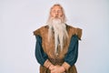 Old senior man with grey hair and long beard wearing viking traditional costume making fish face with lips, crazy and comical