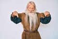 Old senior man with grey hair and long beard wearing viking traditional costume pointing down with fingers showing advertisement,